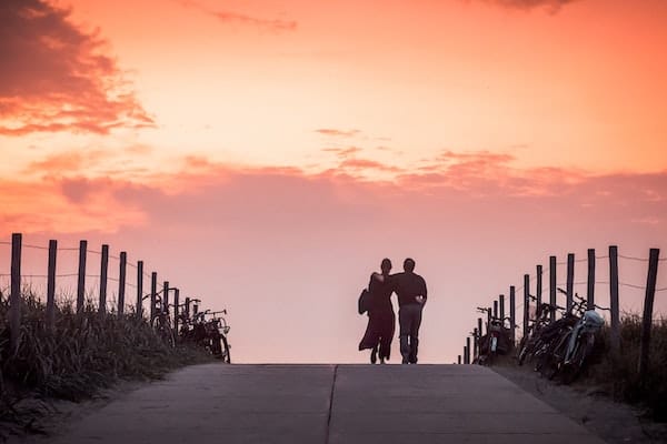 Dieses Bild zeigt einen Mann und eine Frau, die in einen Sonnenuntergang eng umschlungen gehen.