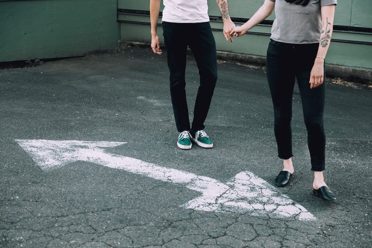 Dieses Bild zeigt ein Paar, dass sich an den Händen hält. Jedoch möchter jeder in eine andere Richtung laufen. Auf dem Bild sind nur die Unterkörper der Personen zu sehen.